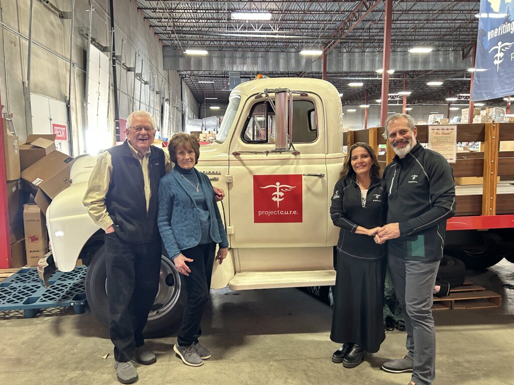 Dr. James Jackson standing with Dr. AnnaMarie Jackson across from Dr. Lorena and Dr. Paulo in front of a white Project C.U.R.E. truck called "Miss Annie."