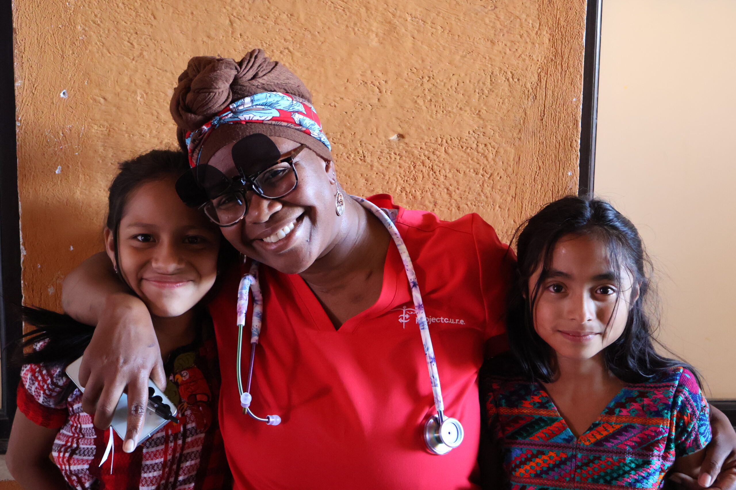 Female physician with arms around two smiling Guatemalan girls during a humanitarian medical clinic outside Antigua, Guatemala.