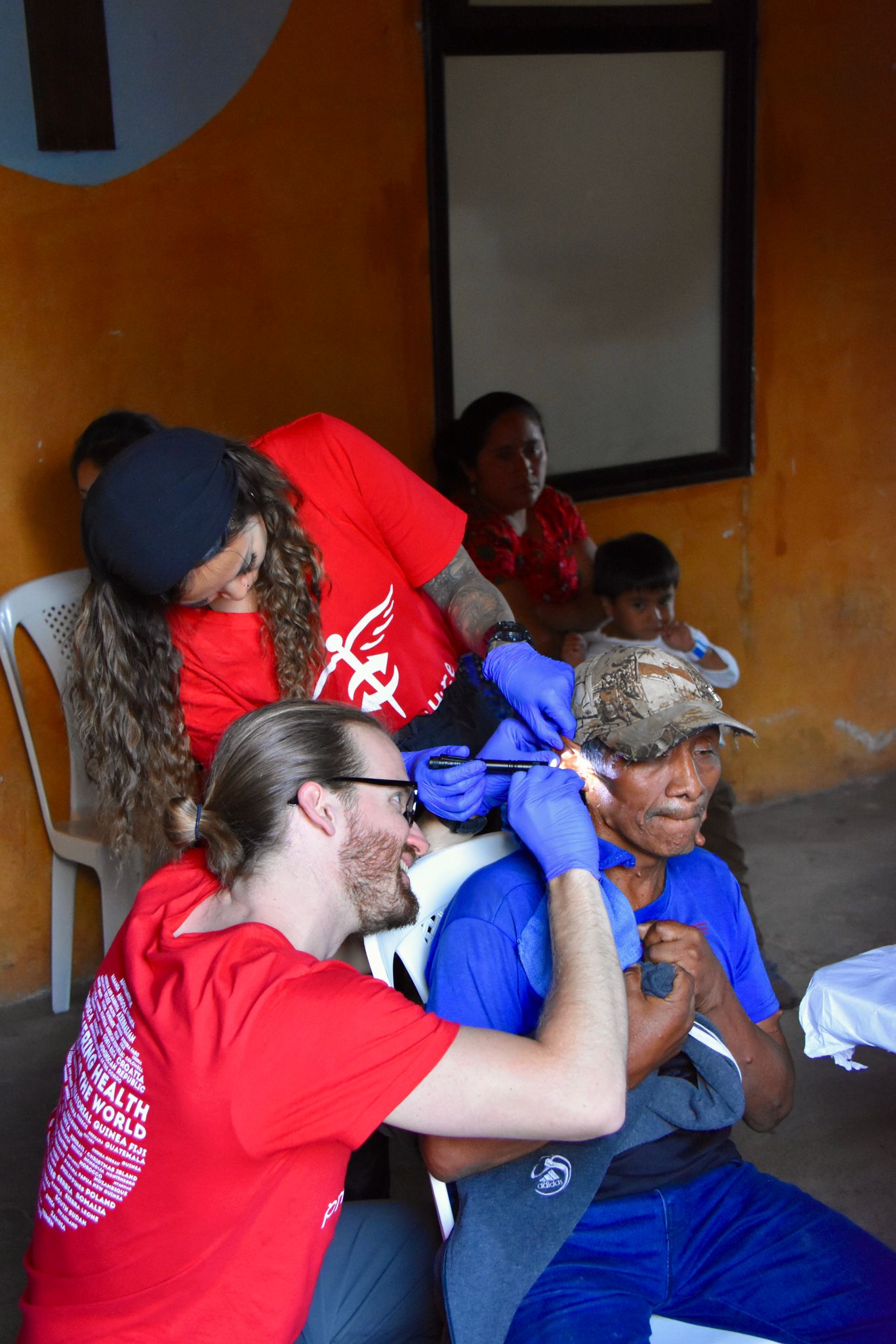 Project C.U.R.E. volunteers carefully removing dried cement from a male patient’s ear during a free clinic in Guatemala.