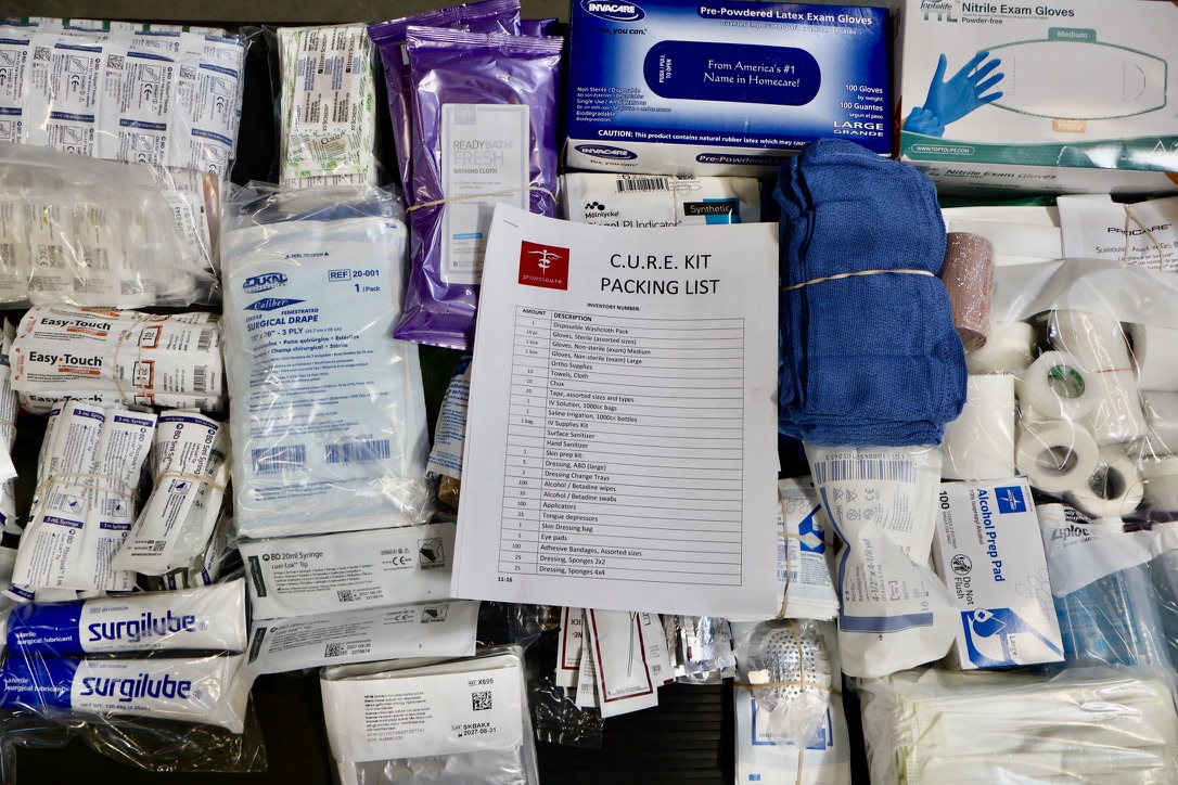Project C.U.R.E. C.U.R.E. Kit packing layout displaying organized medical supplies and packing list, including gloves, gauze, syringes, antiseptics, and wound care items for global health distribution.